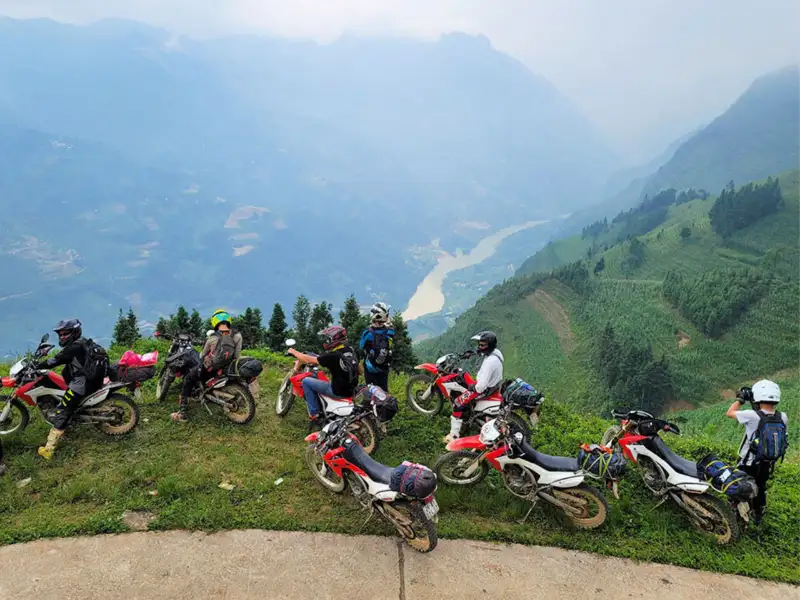 A rider on the Scenic Ha Giang Motorbike Routes, overlooking Ma Pi Leng Pass with limestone peaks and misty valleys in morning light.